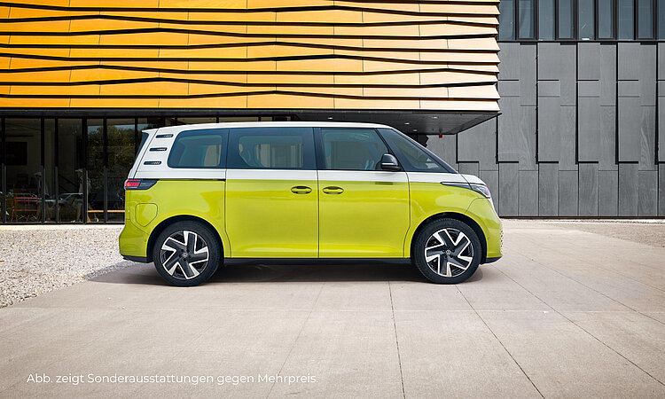 Ein zweifarbiger VW ID.Buzz (oben weiß und unten gelb) steht vor einem futuristischen Gebäude bestehend aus Glas, orangenem Vordach und schwarzen Wänden. Unten links im Bild steht der Hinweis: "Abb. zeigt Sonderausstattungen gegen Mehrpreis".