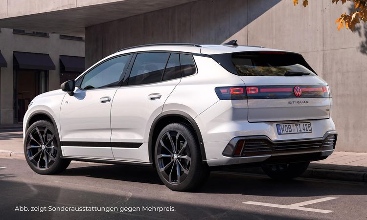 Weißer Volkswagen Tiguan in Heckseitenansicht vor einem modernen Gebäude mit heller Fassade.