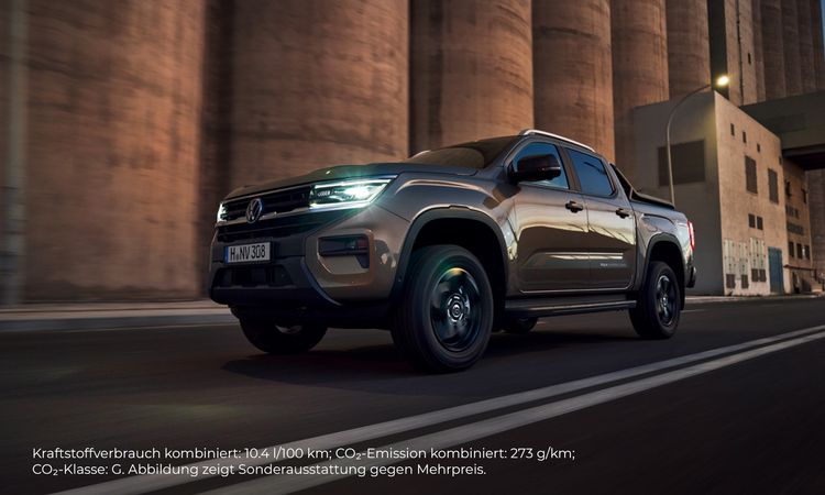 Ein brauner Volkswagen Amarok fährt auf einer Straße in Fahrtrichtung links. Im Hintergrund ist Fabrikgelände, die Farbgebung ist bräunlich. 