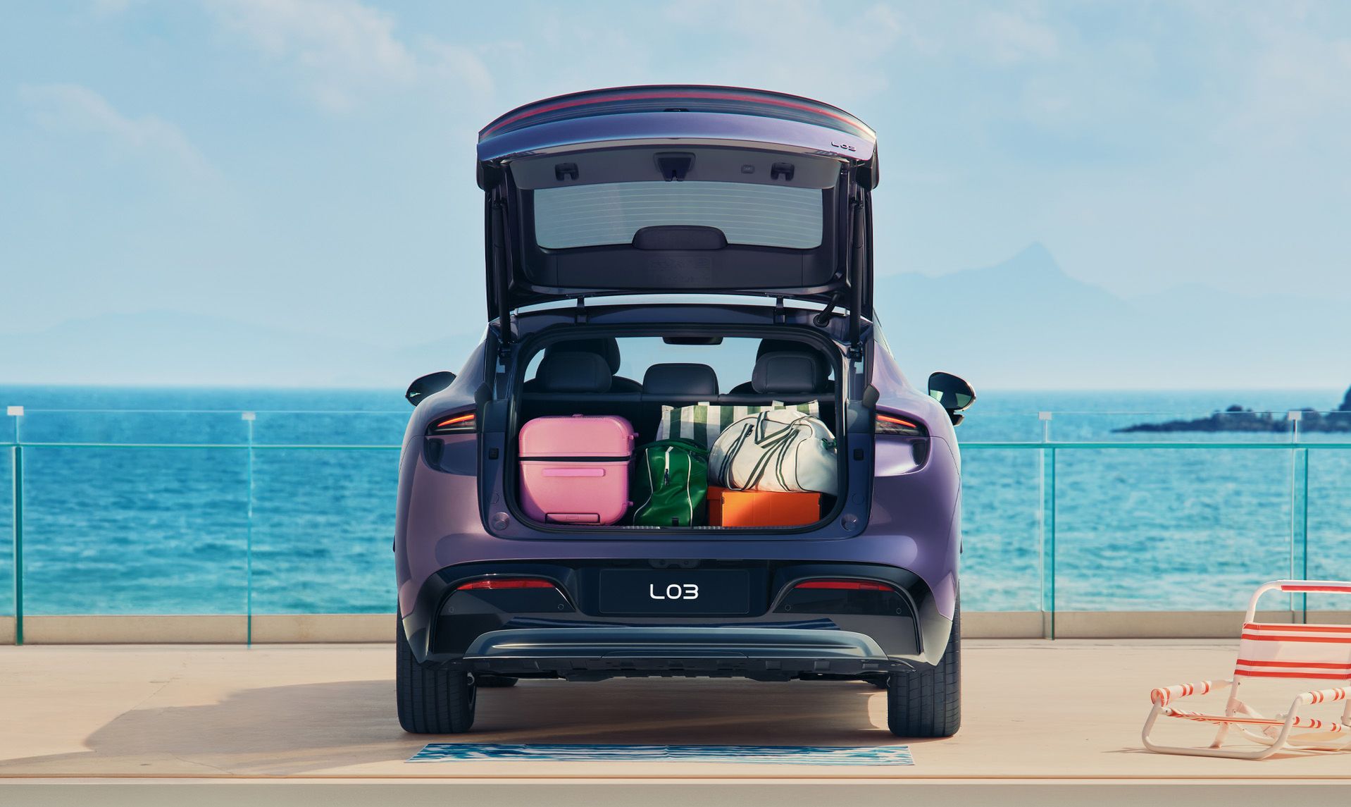 Ein violetter XPENG L03 mit geöffneter elektrischer Heckklappe an einer Strandpromenade. Im Kofferraum stehen Koffer und Taschen, im Hintergrund das Meer.
