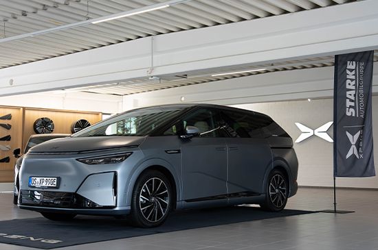 Grauer XPENG X9 Van mit Osnabrücker Kennzeichen im STARKE Showroom, daneben eine STARKE Automobilgruppe Flagge mit XPENG Logo.