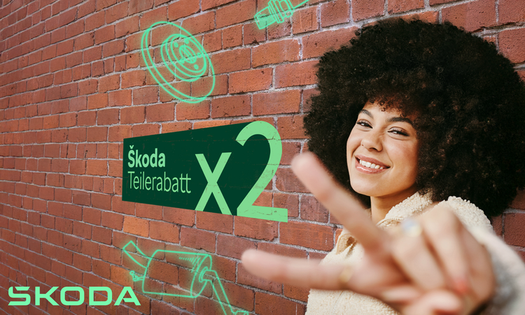 Eine Frau mit dunklen starken Locken hät eine "2" mit den Fingern in die Kamera. Im Hintergrund ist eine rote Backsteinmauer an der Skoda Teilerabatt x2 steht. 