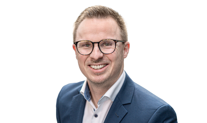 Portrait eines Mitarbeiters mit kurzem Haar und Brille in einer weißen Jacke.