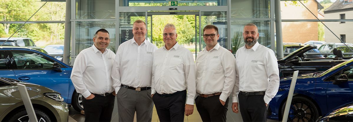 Mehrere Mitarbeitende in einem Fahrzeugshowroom zwischen ausgestellten Pkw-Modellen.