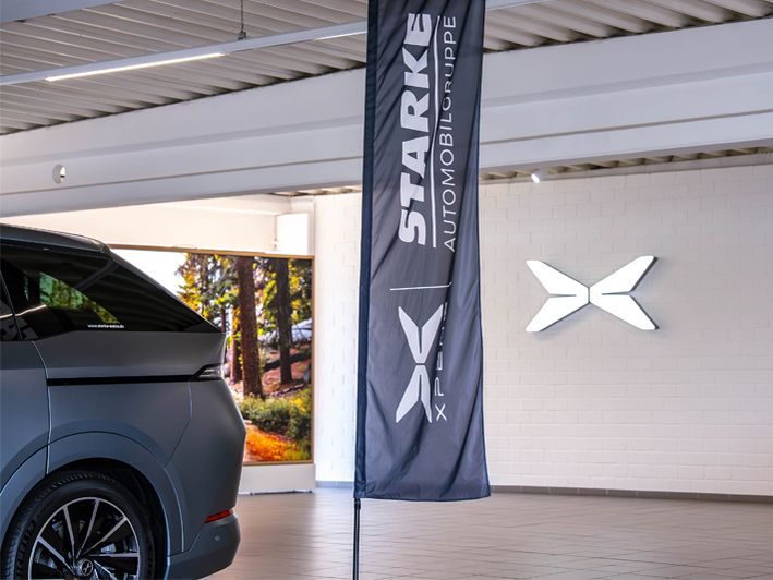 XPENG X9 in einer Ausstellungshalle mit STARKE Automobilgruppe Fahne und beleuchtetem XPENG Markenlogo an der Wand.