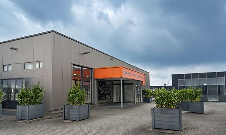 Eingangsbereich eines XPENG Showrooms mit orangefarbener Fassadenverkleidung, XPENG Markenlogo und bepflanzten Kübeln.