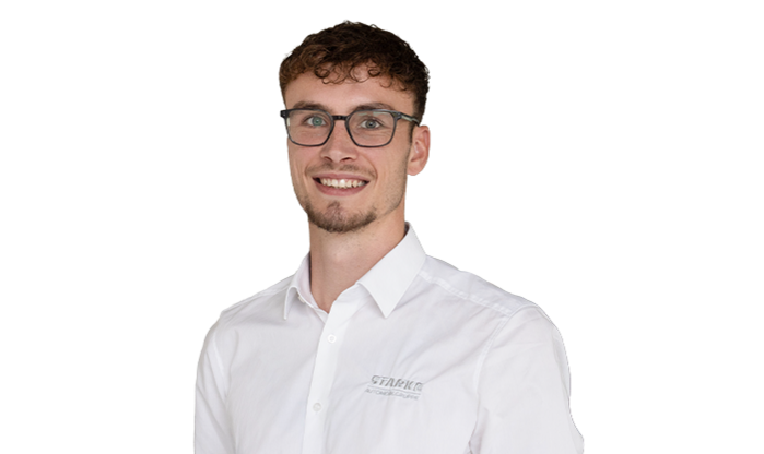 Ein junger Mann mit braunem Haar trägt eine Brille und ein weißes STARKE Hemd.
