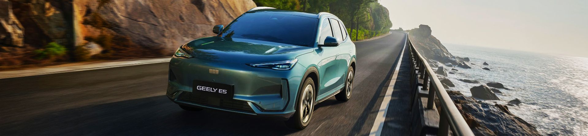 Vollelektrischer Geely E5 fährt auf einer geschwungenen Küstenstraße entlang steiler Felsen mit Blick auf das Meer.