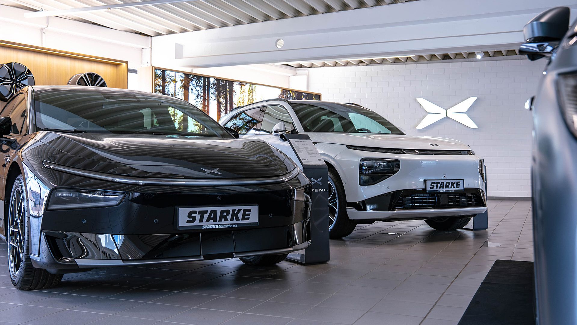 Schwarzer XPENG P7 und weißer XPENG G9 mit STARKE Kennzeichen im Ausstellungsraum eines STARKE XPENG Stores, im Hintergrund das XPENG Logo an der Wand.