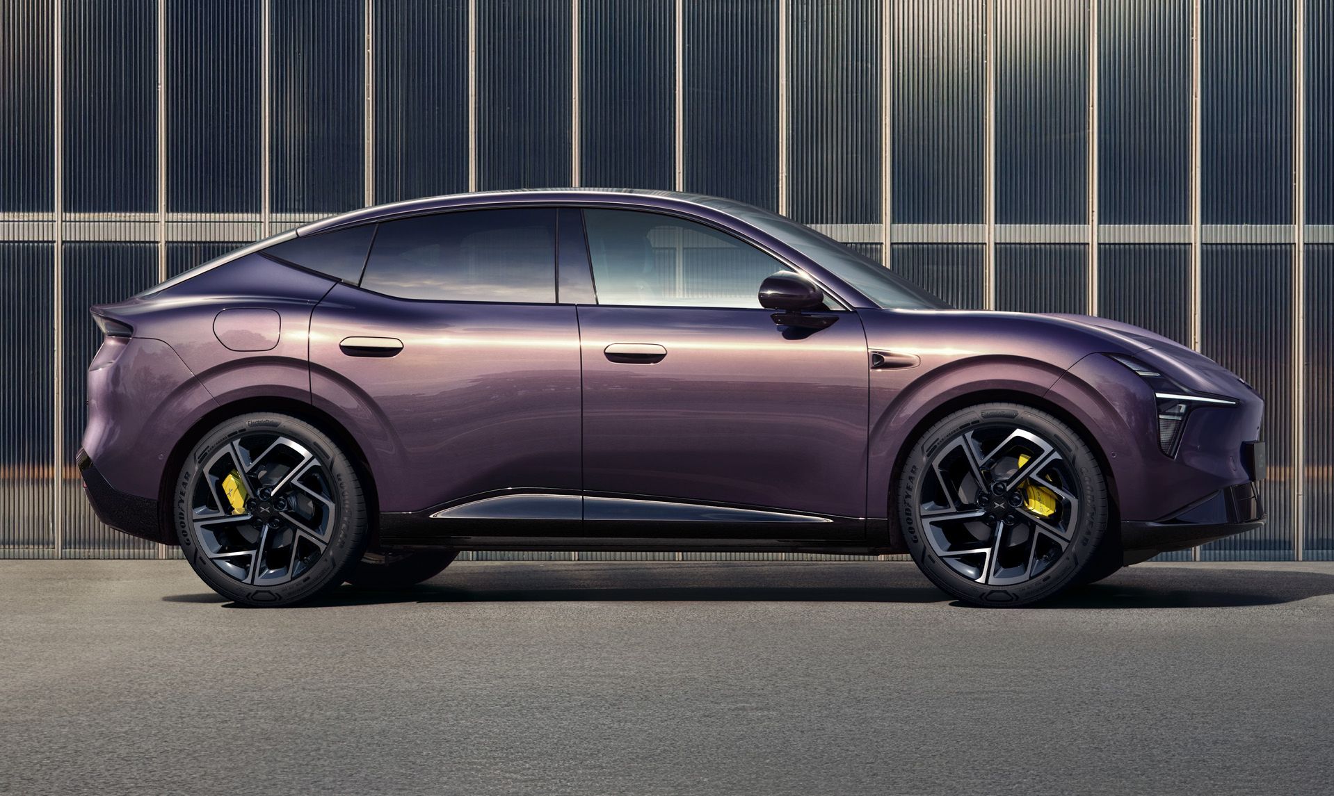 Ein violetter XPENG L03 in der Seitenansicht vor einer modernen Fassade aus Metall und Glas. Die fließende Dachlinie des SUV-Coupés ist deutlich zu erkennen.