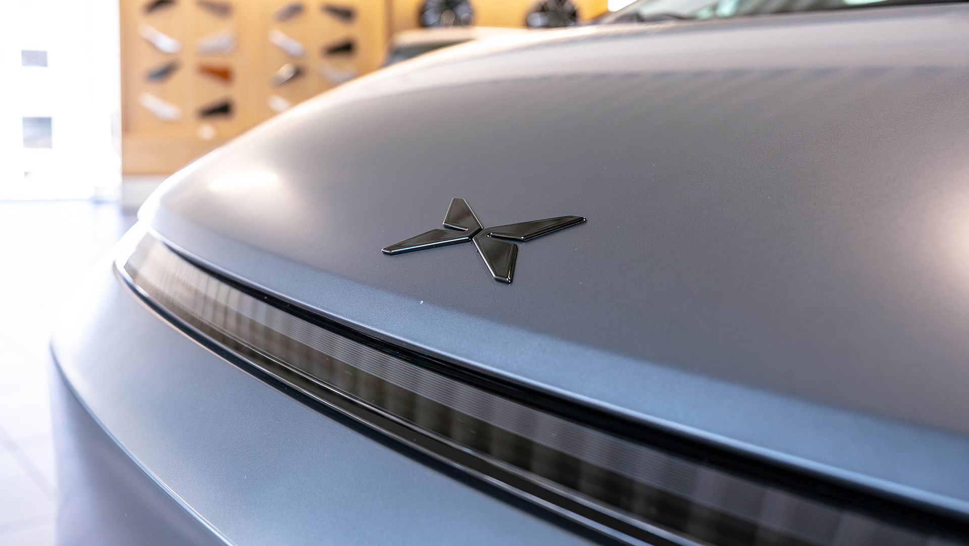 Nahaufnahme des XPENG Logos auf der matt-grauen Motorhaube eines XPENG Fahrzeugs im STARKE Showroom.