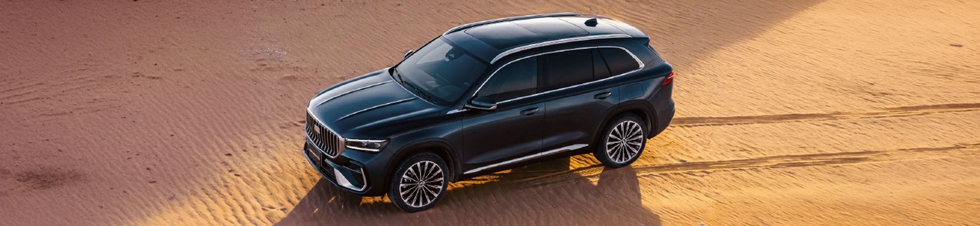 Geely Monjaro EM-i in dunkelgrauer Lackierung aus erhöhter Perspektive auf einer Sanddüne mit Reifenspuren.