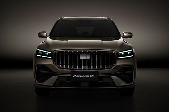 Geely Monjaro EM-i in bronzefarbener Lackierung in Frontansicht mit beleuchteten Scheinwerfern vor dunklem Hintergrund.
