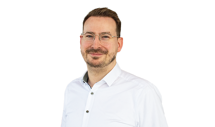 Portrait eines Mitarbeiters mit kurzem Haar, Brille und Bart im weißen Hemd.