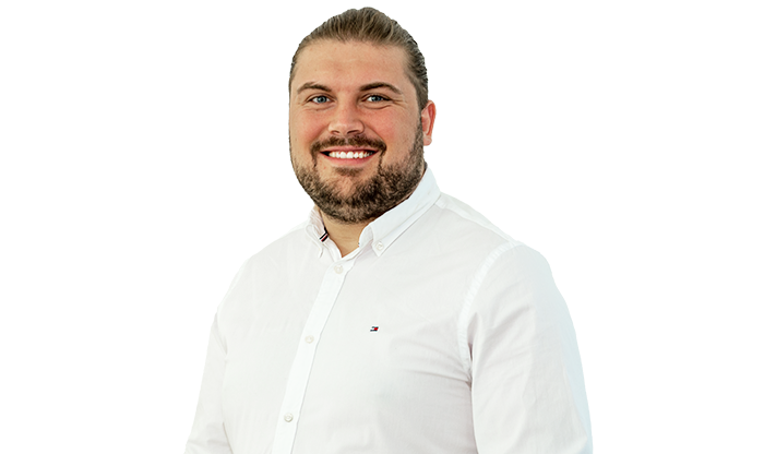 Porträt eines Mitarbeiters mit kurzen Haaren, einem Bart und weißem Hemd. 