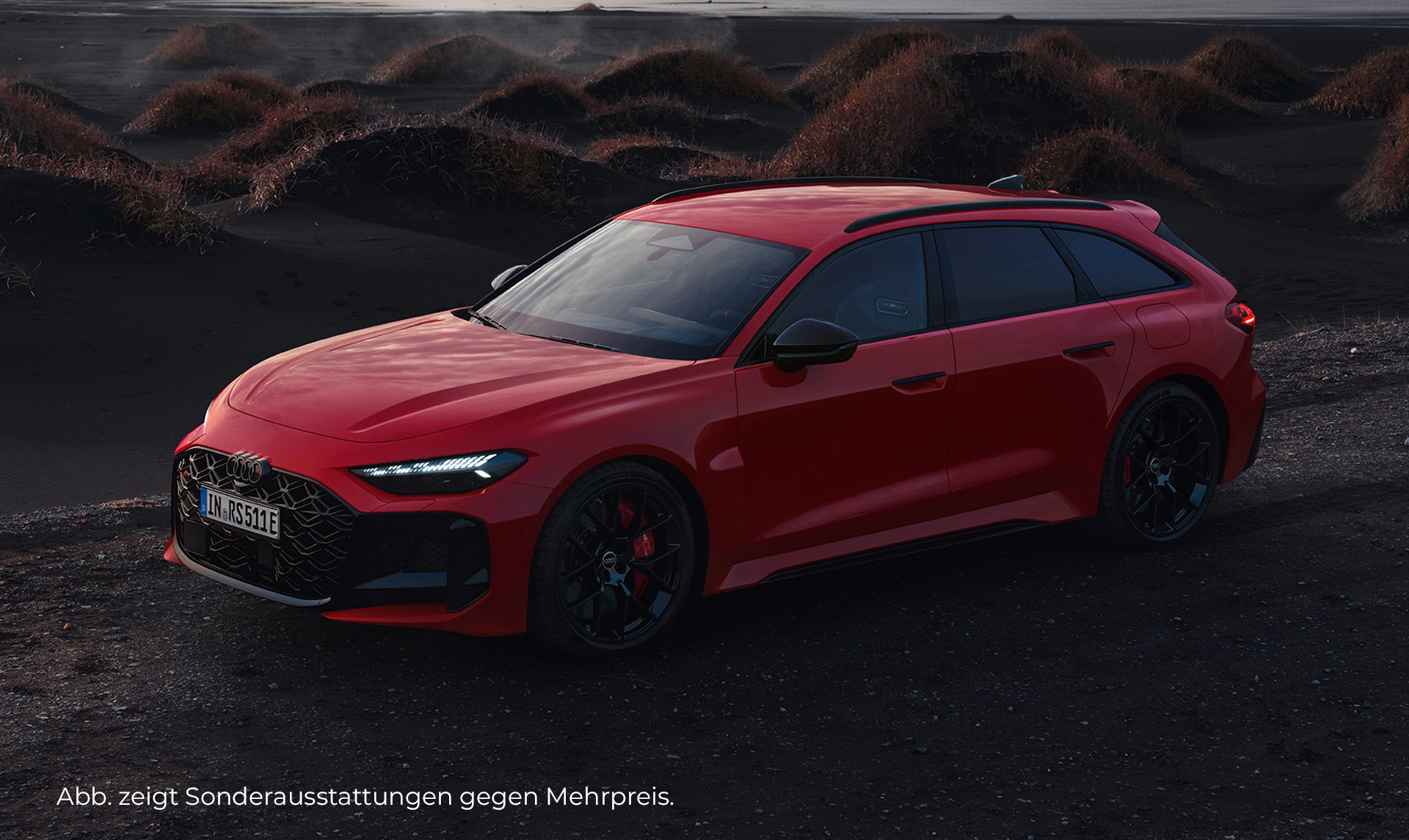 Roter Audi RS 5 Avant performance Plug-in-Hybrid in einer dunklen, hügeligen Landschaft bei Dämmerung.