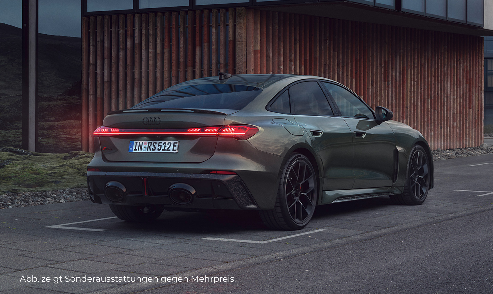 Audi RS 5 Limousine in dunklem Grün, von hinten schräg fotografiert, vor einem modernen Gebäude bei Dämmerung.