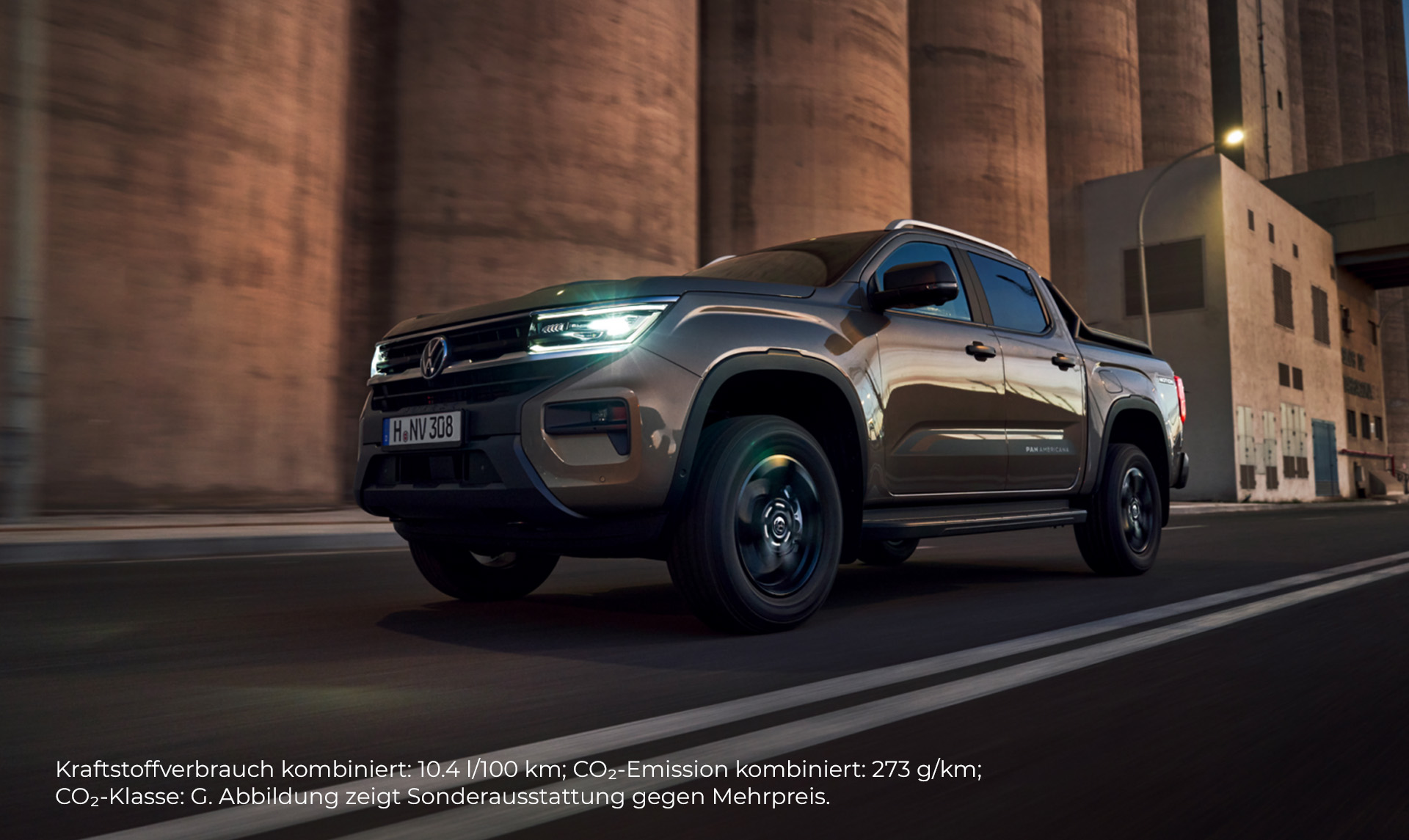 Ein brauner Volkswagen Amarok fährt auf einer Straße in Fahrtrichtung links. Im Hintergrund ist Fabrikgelände, die Farbgebung ist bräunlich. 