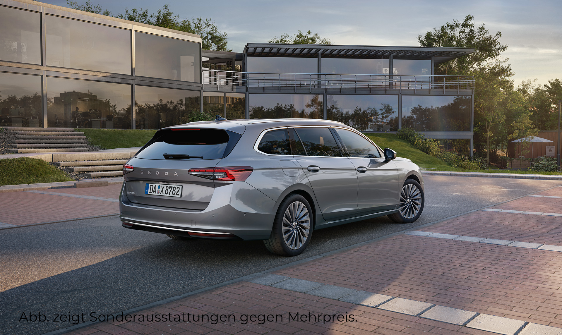 Das Bild zeigt einen grauen Skoda Suberb der auf einem Parkplatz vor einem modernen Bürogebäude aus Glas steht. Zu sehen ist die Heckansicht und die rechte Fahrzeugseite.