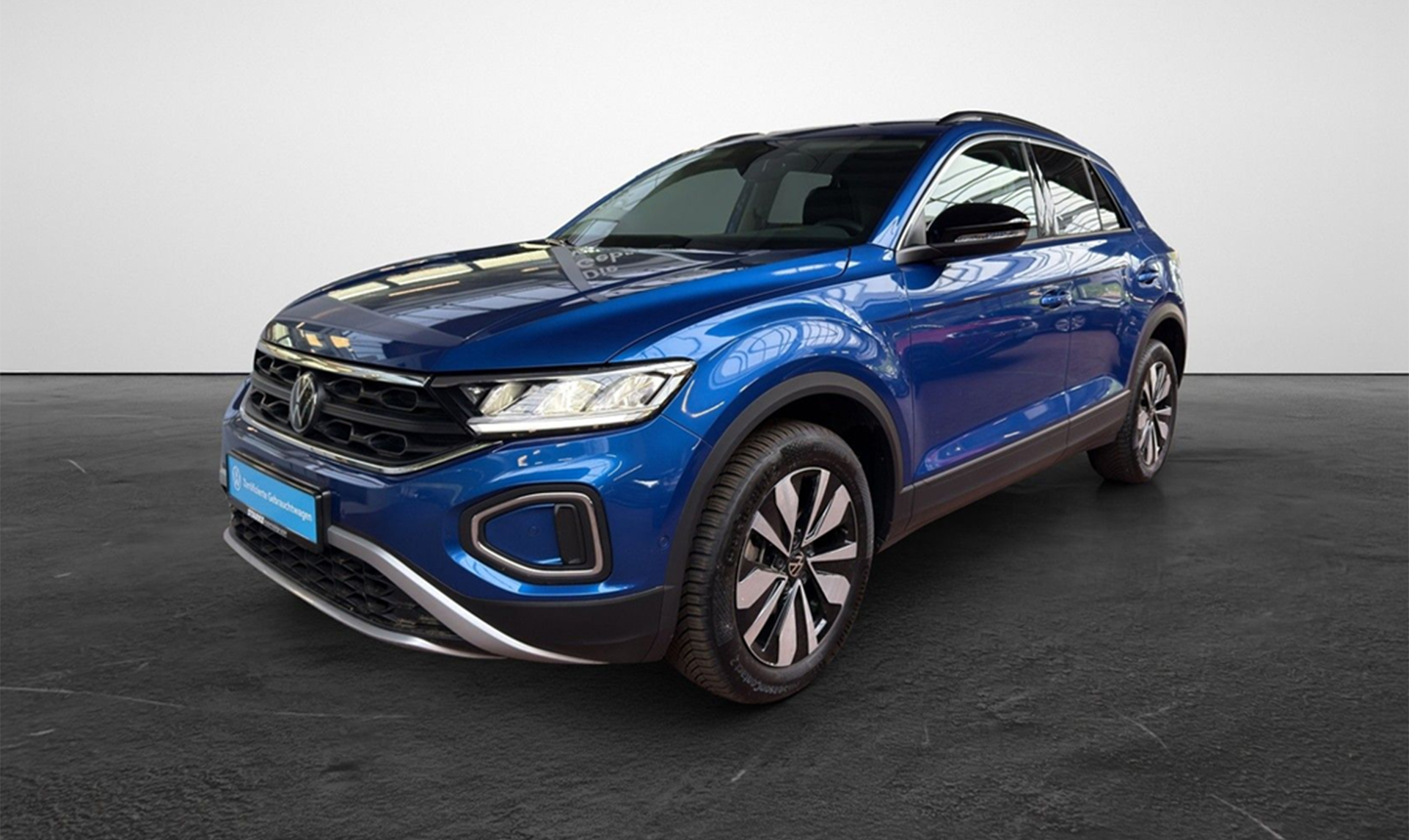 Blauer Volkswagen T-Roc in Frontseitenansicht, fotografiert in einer Fahrzeughalle mit hellem Hintergrund.