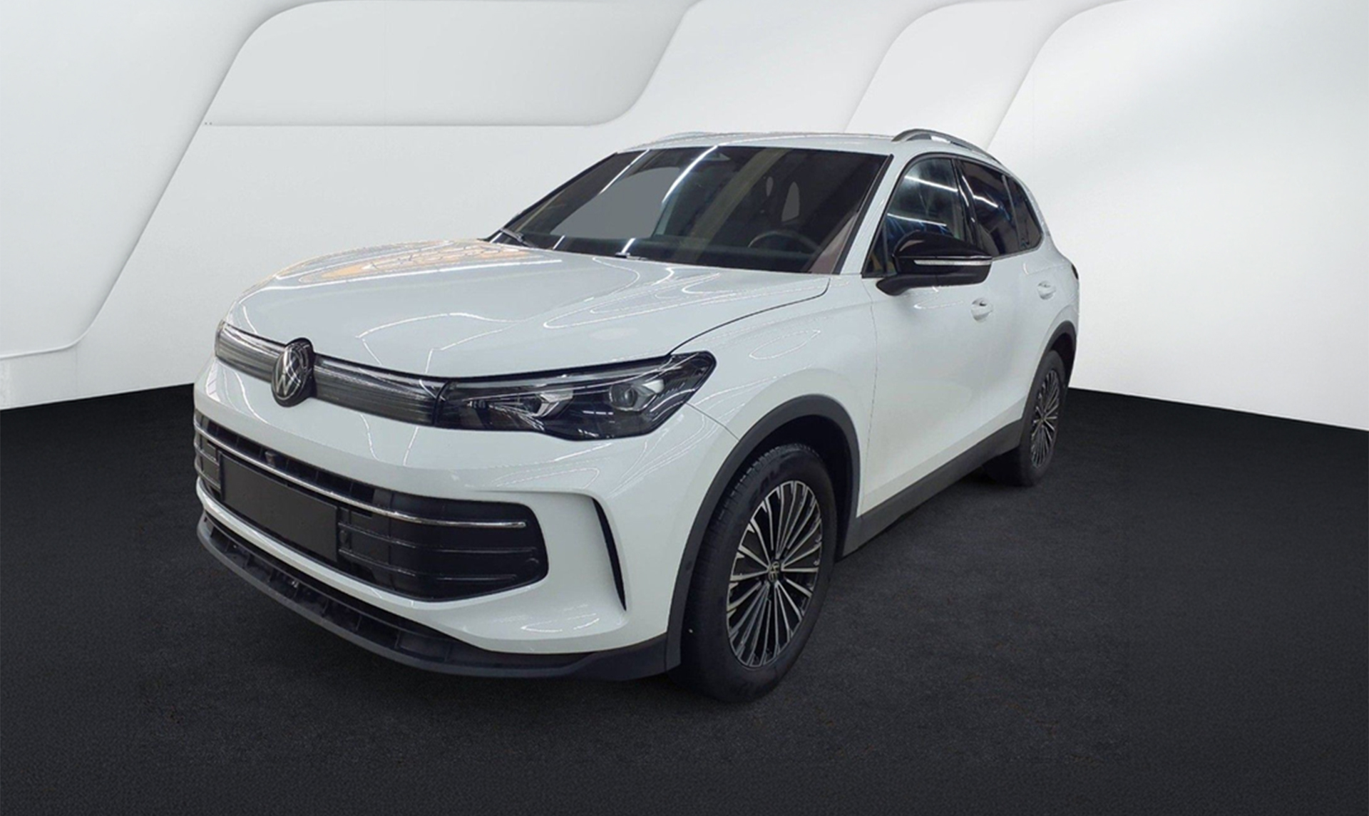 Weißer Volkswagen Tiguan in Frontseitenansicht auf schwarzem Boden in einem hellen Fotostudio.