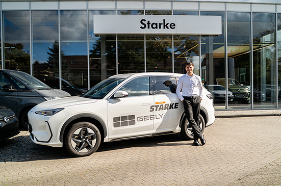 Weißer Geely E5 mit STARKE und GEELY Beschriftung vor einem STARKE Autohaus, ein Mann in weißem Hemd lehnt am Fahrzeug.