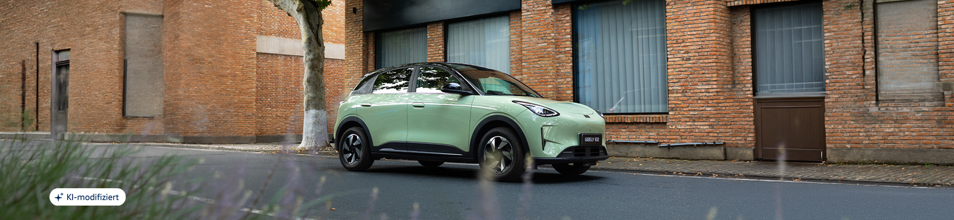 Geely E2 in hellgrüner Lackierung vor einem Gebäude mit Backsteinfassade in urbaner Umgebung.