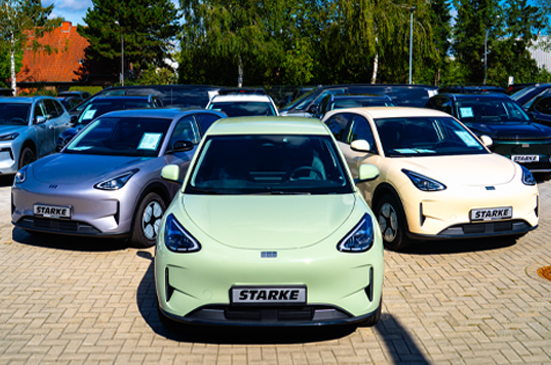 Drei Geely E2 in unterschiedlichen Lackierungen auf einem Fahrzeugplatz, mit weiteren Geely E5 und Geely Starray EM-i Modellen im Hintergrund.