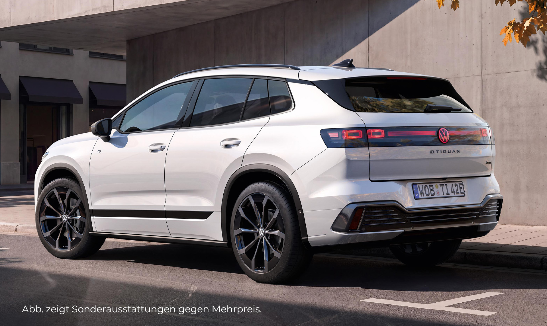Weißer Volkswagen Tiguan in Heckseitenansicht vor einem modernen Gebäude mit heller Fassade.