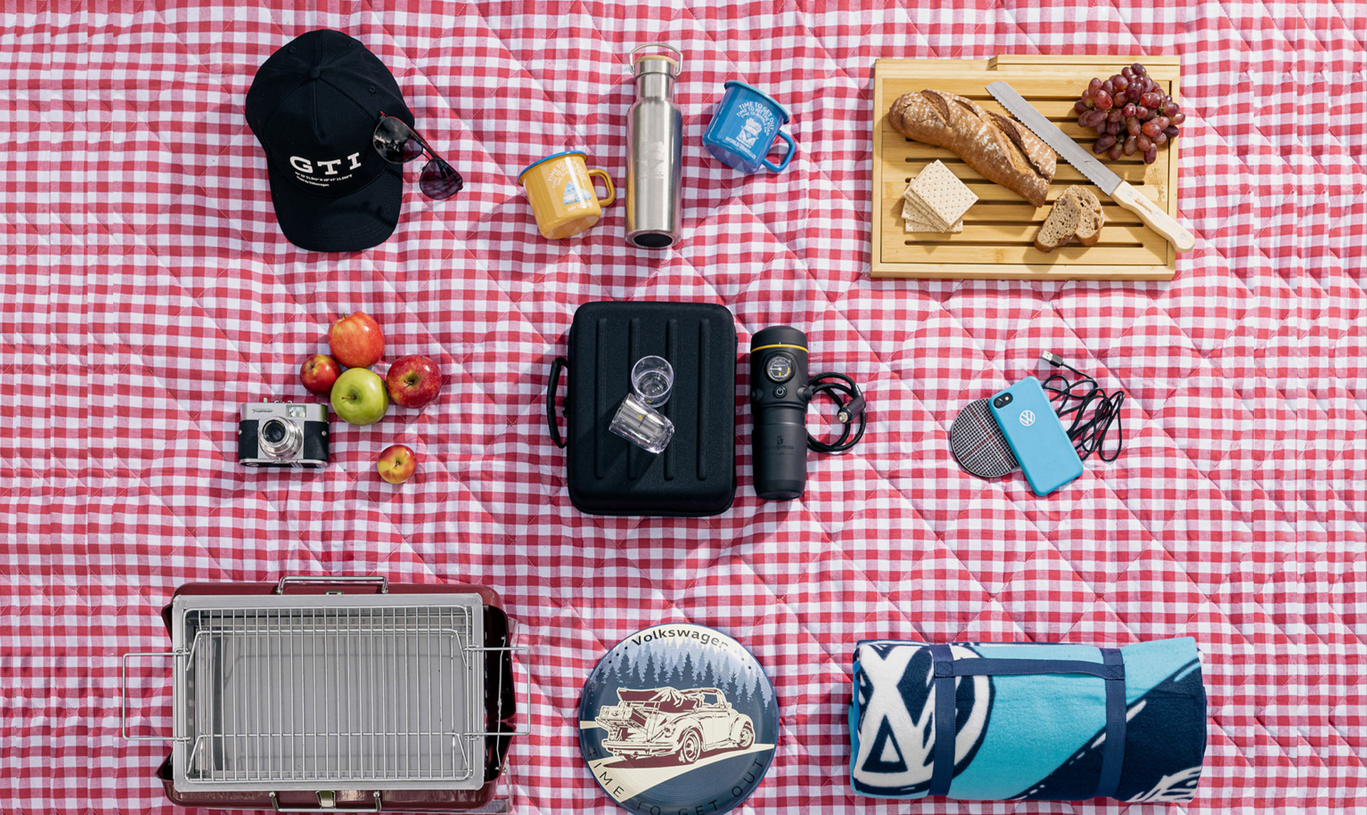 Auf dem Bild ist eine Picknickdecke zu sehen, auf dem verschiedenes Zubehör von Volkswagen liegt, unter anderem eine Cappy. 